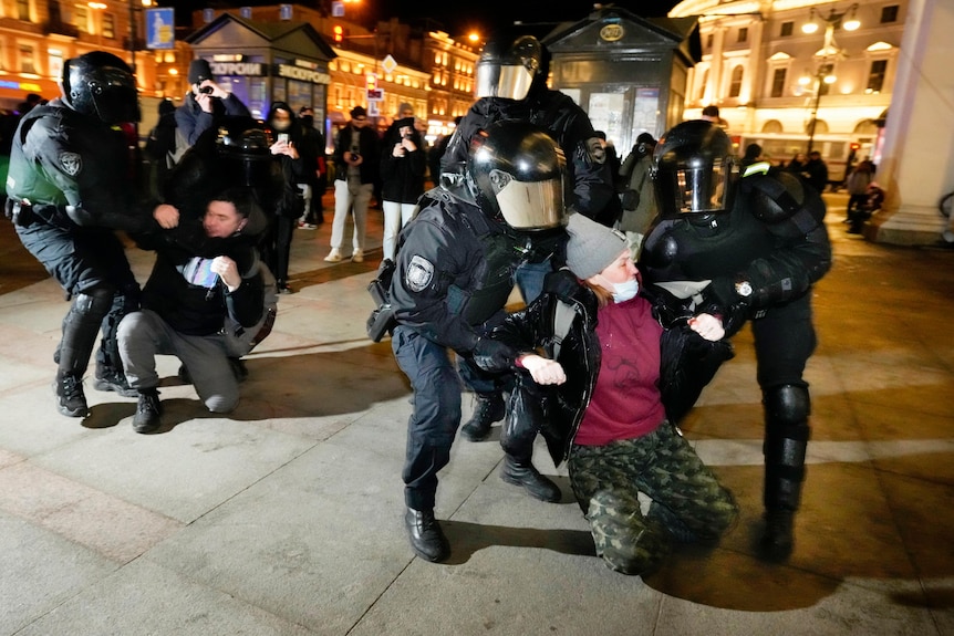 Riot police wearing helmets and armoour detain young people at a night time demonstration.