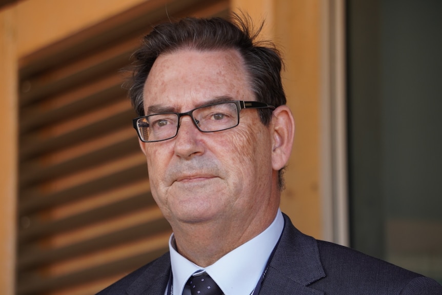 A police officer wearing a dark suit and glasses speaks at a press conference