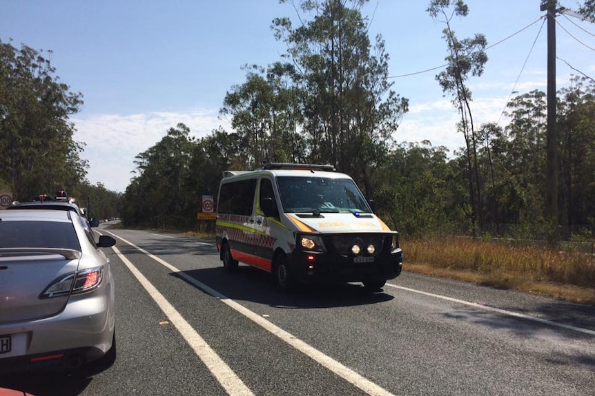 An ambulance on a bitumen road with bushland on the right.