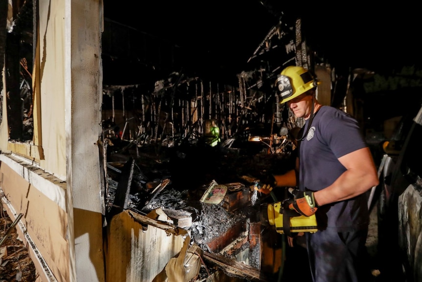 You look through the charred doorway of a fire-ravaged house as a US fireman enters with a yellow torch.