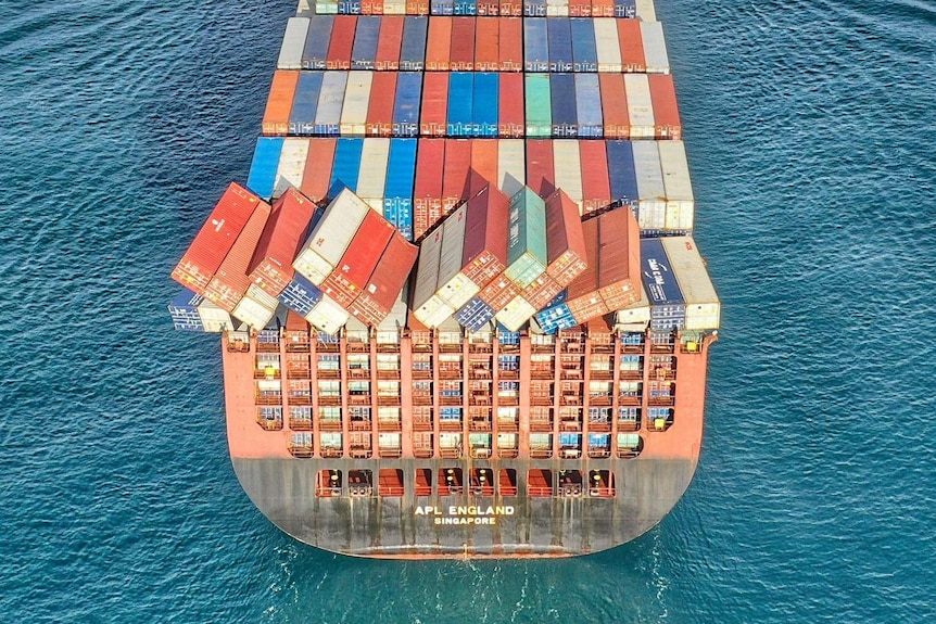 A few containers sit awkwardly atop a cargo ship as if they are about to fall