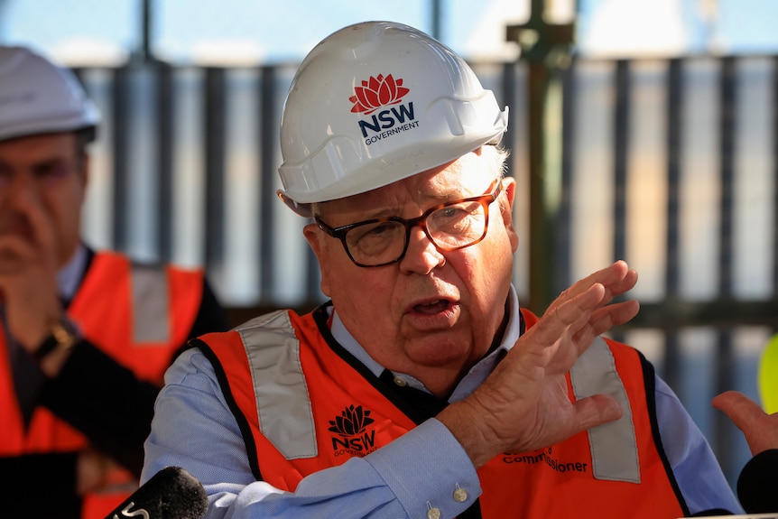 a man wearing a hard hat talking to the press at a construction site
