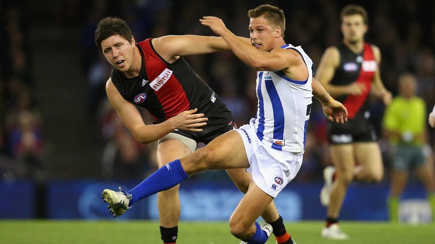 Kangaroos' Andrew Swallow kicks while being tackled by Essendon's Nick O'Brien at Docklands.