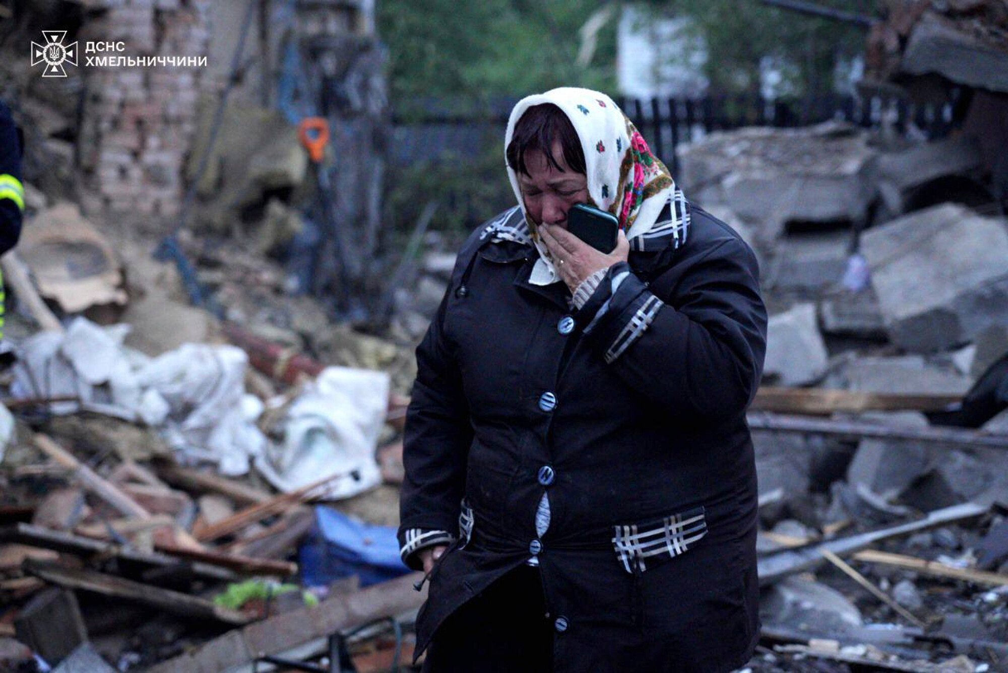 A woman in a headscarf and thick jacket cries as she walks through rubble and debris.