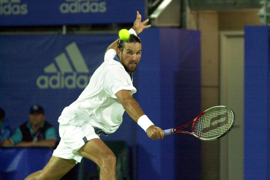 Tennis player Pat Rafter looks at the tennis ball he is stretching to hit with a forehand shot.