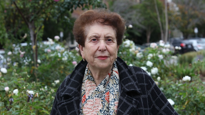 A woman stands in front of a rose garden.