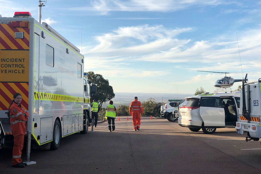 Emergency vehicles in a remote bush car park with a helicopter hovering low overhead.