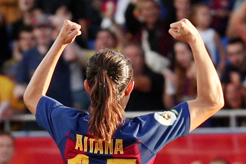 A female soccer player raises her arms in triumph in front of a crowd.
