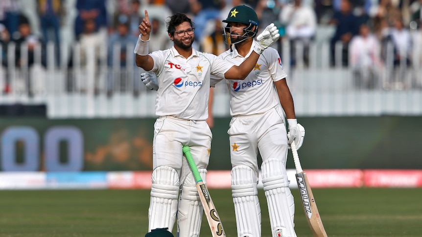 A bespectacled Imam-Ul-Haq has his helmet off and is holding his arms up