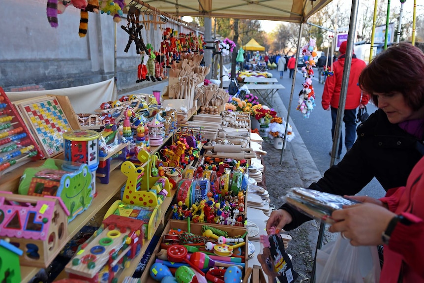 Woman looks at wooden toys sold at pop up stall outside Brodno Cemetery