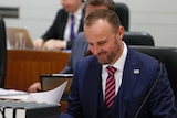 Andrew Barr smiles as he looks at papers in the ACT Legislative Assembly.