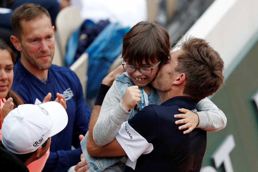 A smiling boy hugs his tennis player dad at the French Open.