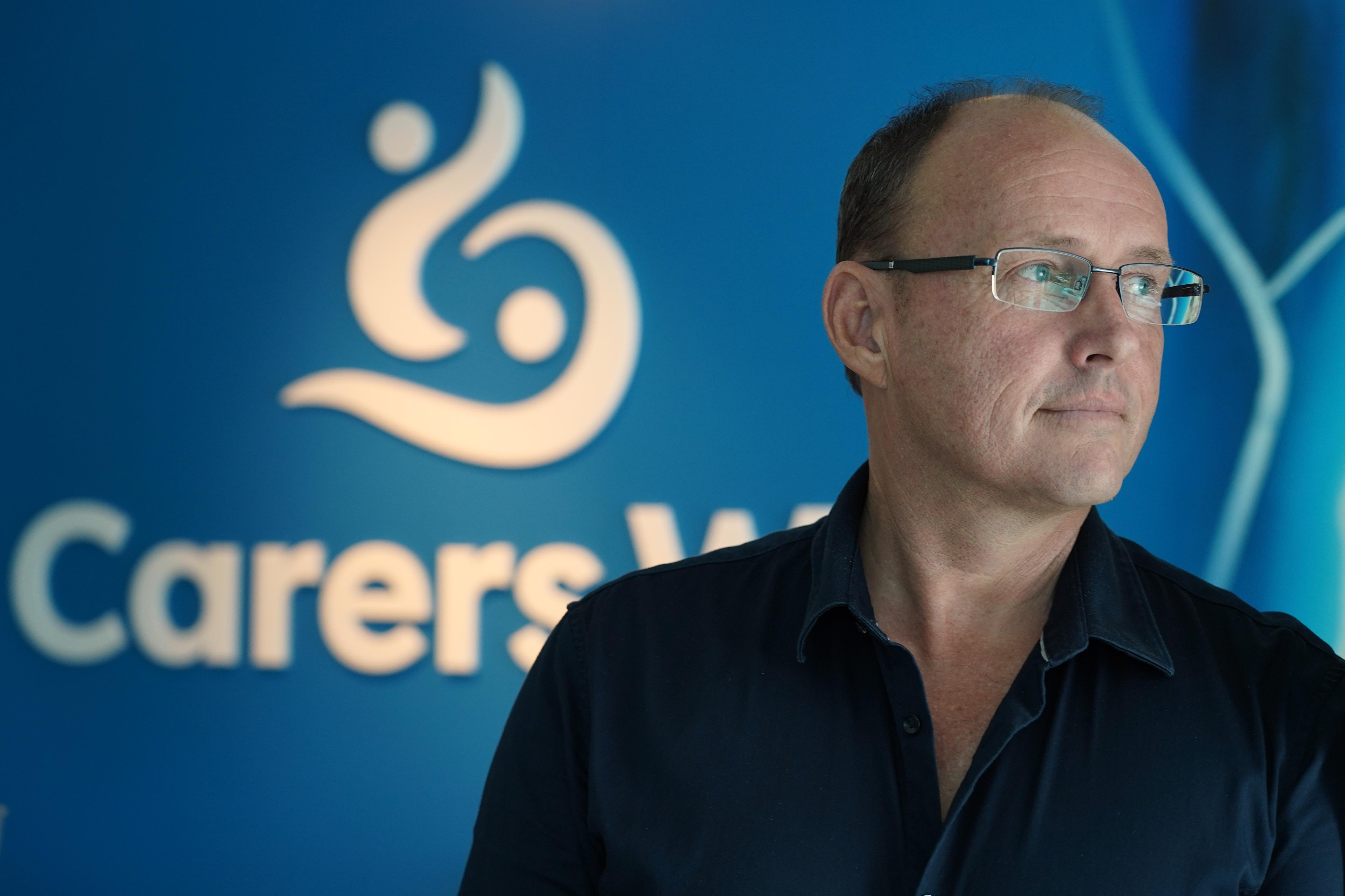 Un hombre con camisa negra y gafas mira hacia un lado 