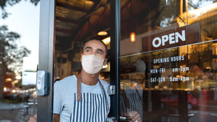 Waiter looking out the door of a cafe wearing a face mask