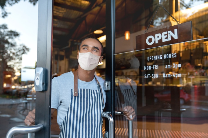 Waiter looking out the door of a cafe wearing a face mask