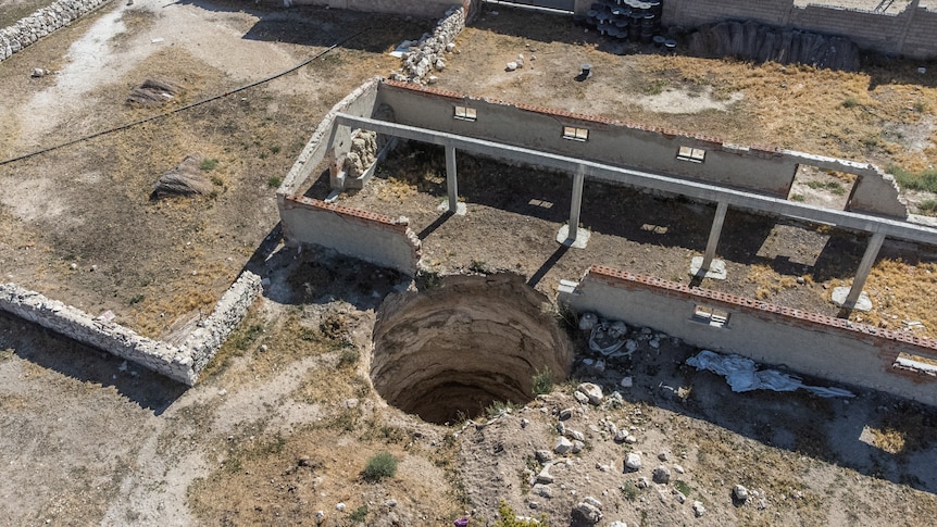 An aerial shot shows a large sinkhole next to an old shed with its roof removed.