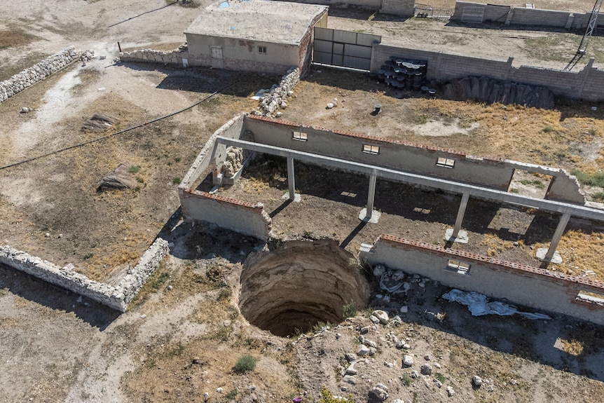 An aerial shot shows a large sinkhole next to an old shed with its roof removed.