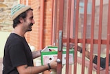A man wearing a beanie hands over a box of food.
