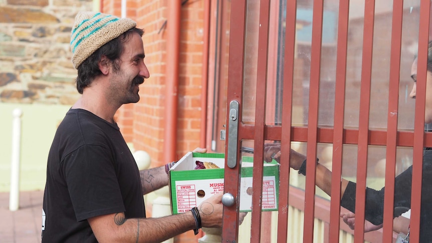 A man wearing a beanie hands over a box of food.