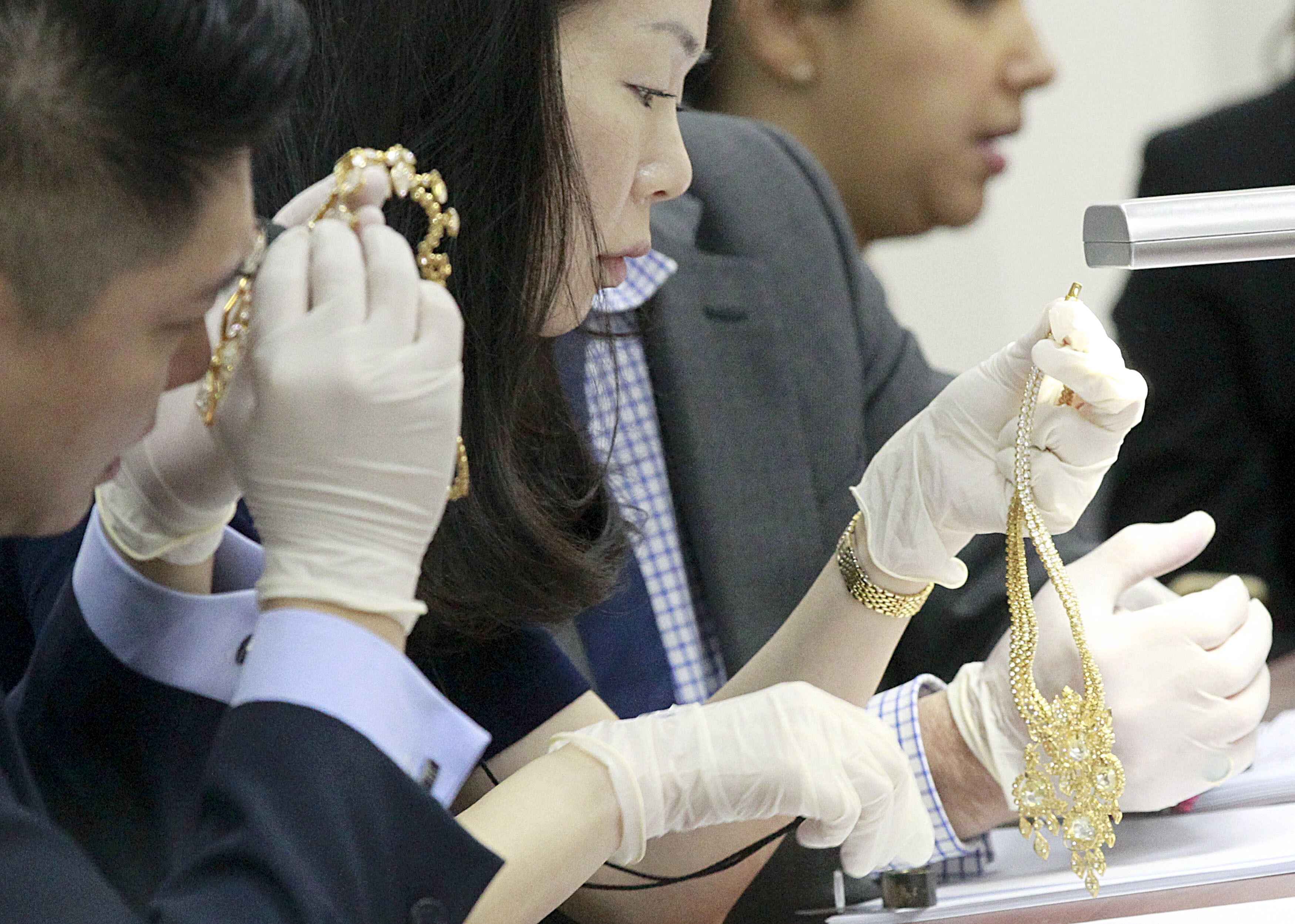 Three people in gloves inspecting bejewelled necklaces 
