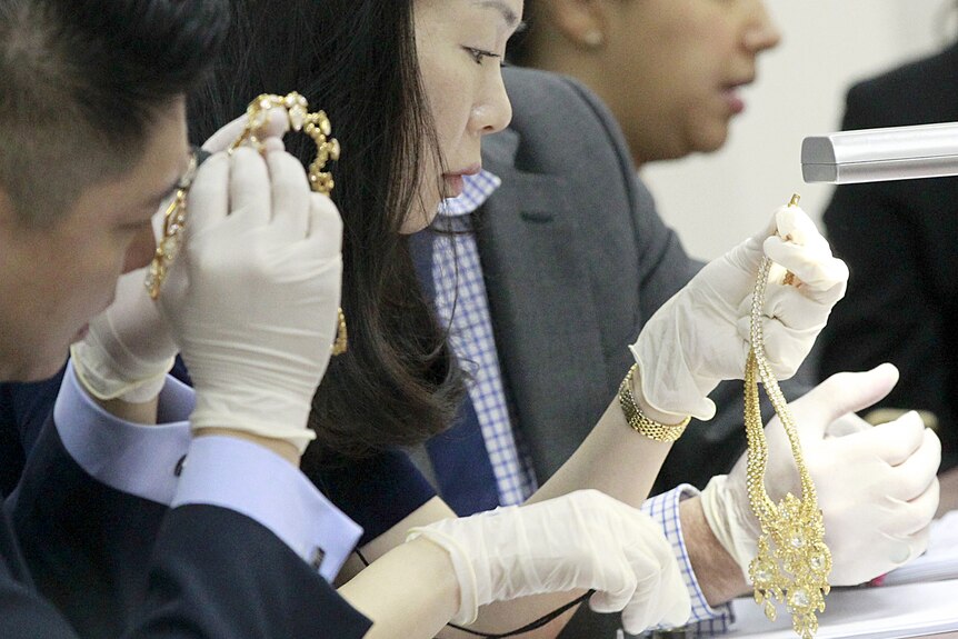 Three people in gloves inspecting bejewelled necklaces 