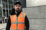Neil Erikson wears an orange Toll Holdings vest outside the Federal Court.