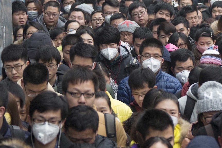 A crowd of commuters line up outside a train station, many wearing face masks to protect against smog