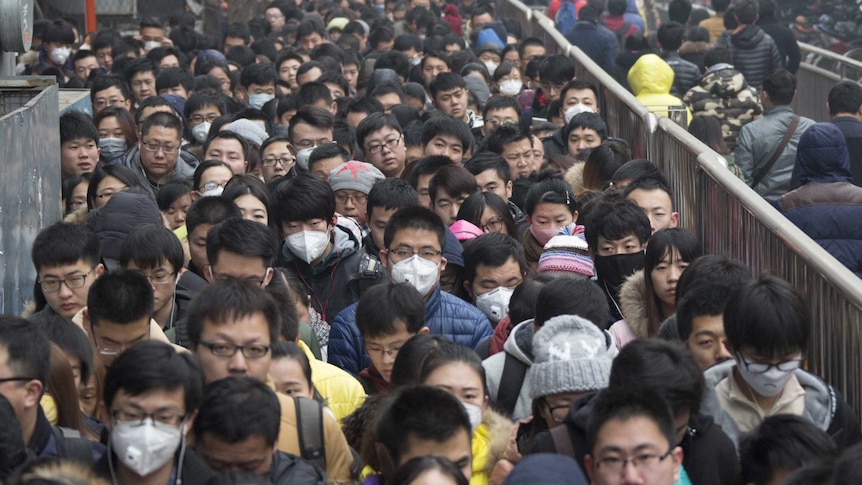 A crowd of commuters line up outside a train station, many wearing face masks to protect against smog