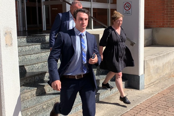 A young man in a blue suit walks down the steps of a building