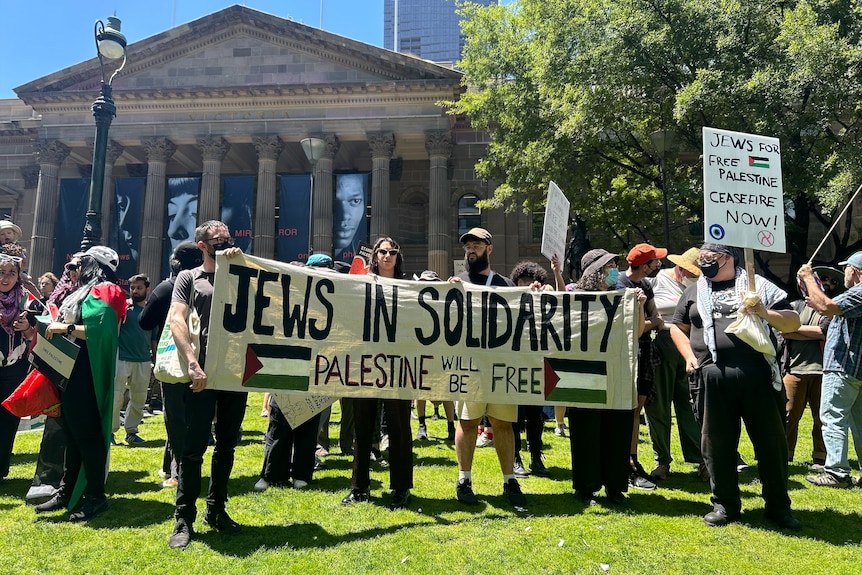 People hold a banner saying 'Jews for in solidarity, Palestine will be free' at a rally.