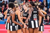 A group of dejected Collingwood Super Netball players gather together on court after a loss.