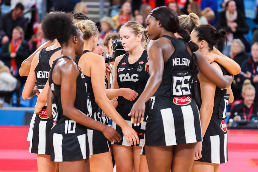 A group of dejected Collingwood Super Netball players gather together on court after a loss.