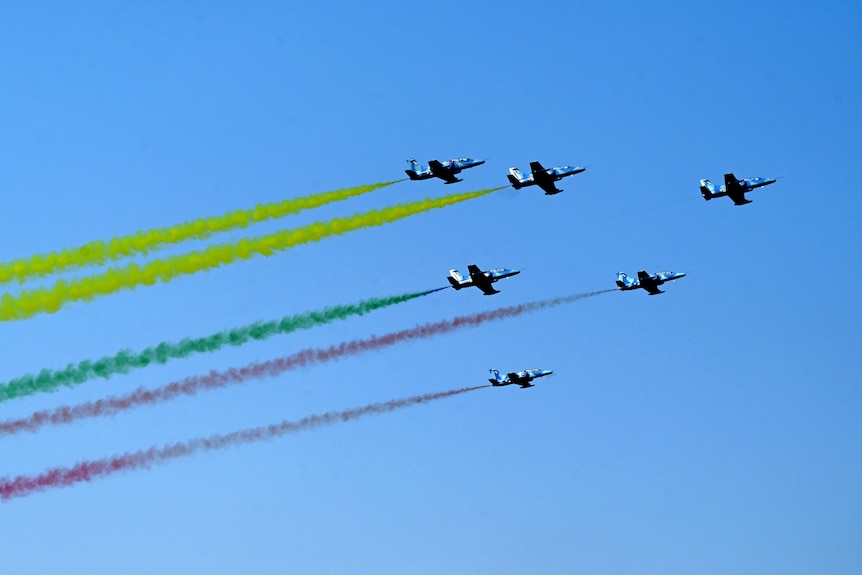 Jets fly in blue sky with yellow, green and red contrails, the colours of Myanmar's flag.