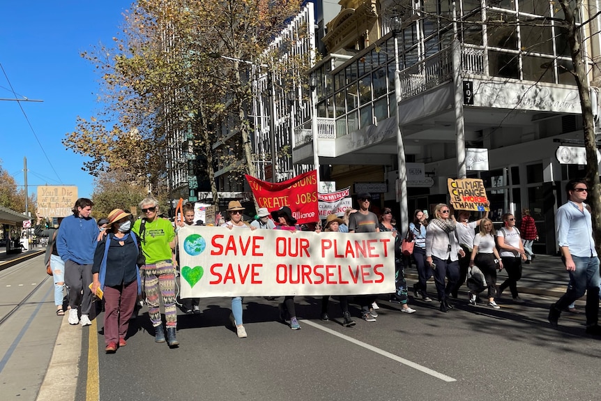 A group of protesters carrying signs and banners marches through Adelaide's CBD.