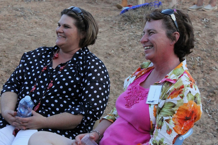Two women smiling and sitting on chairs in a drought-affected region