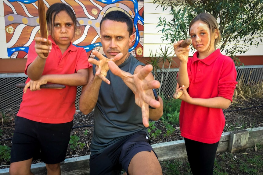 A man gestures at the camera in a pose with two students holding clap sticks