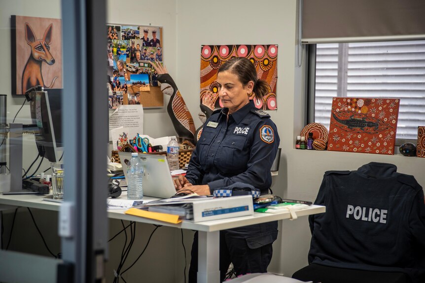 A woman wearing a police uniform in an office filled with Aboriginal art types on a computer.