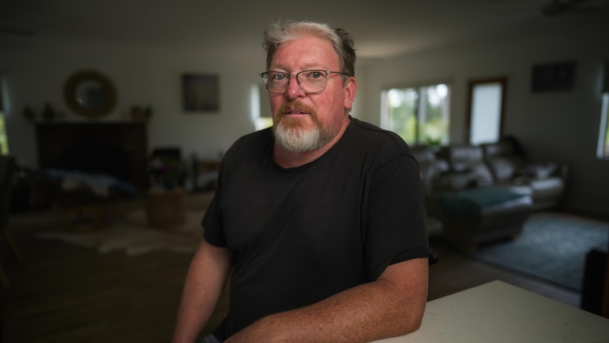 Man wearing a black shirt and glasses sitting at a table.