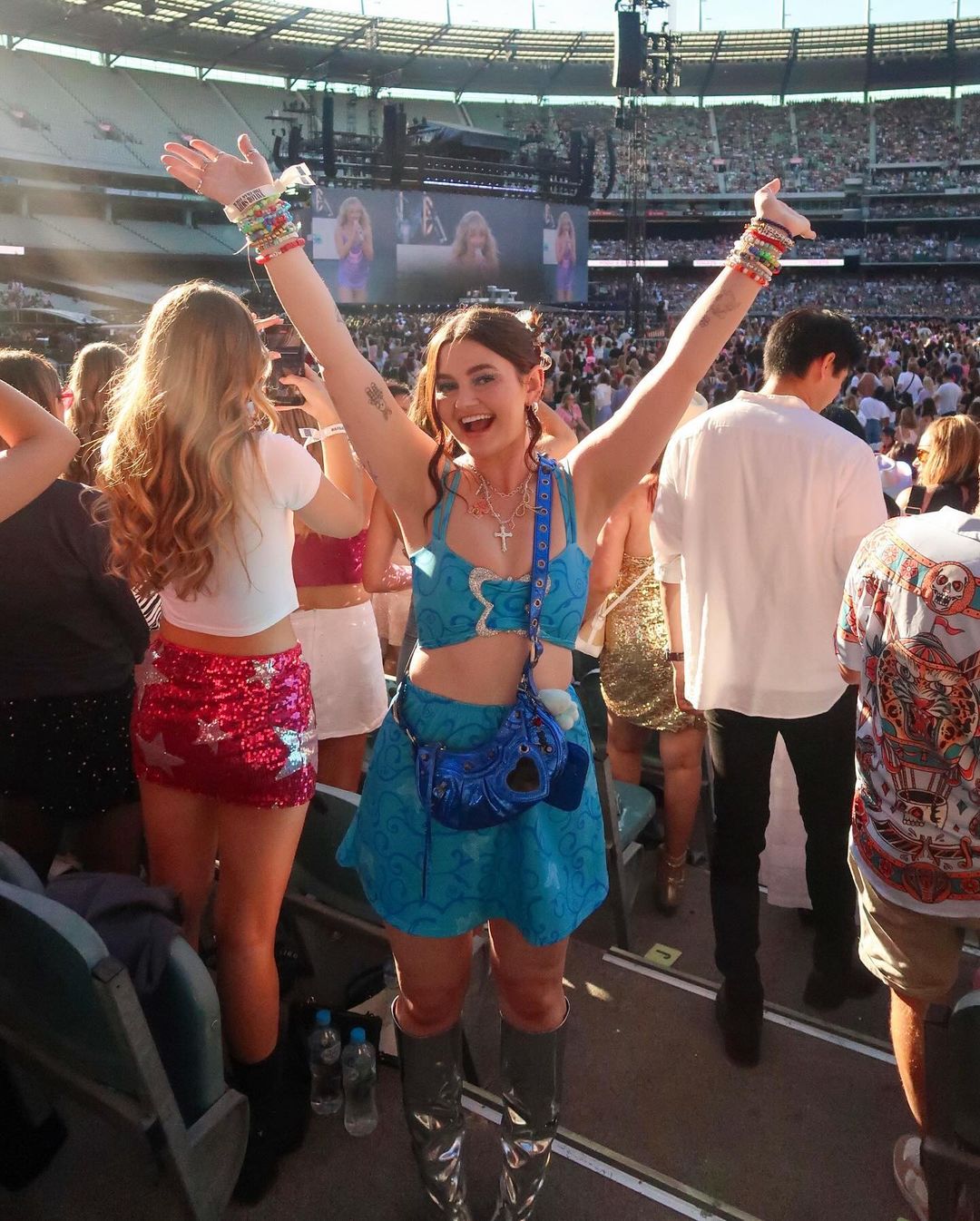 Una joven vestida con un lindo traje azul sonríe y levanta las manos en el aire en el estadio.