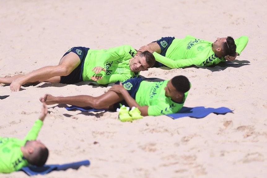 Everton players stretch on the sand while wearing flourescent training shirts