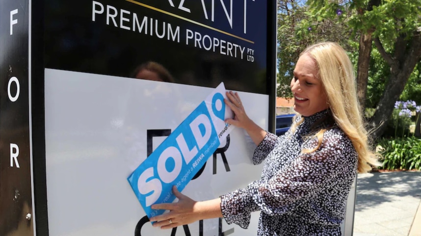 A woman puts a blue sold sticker across a poster of a house for sale