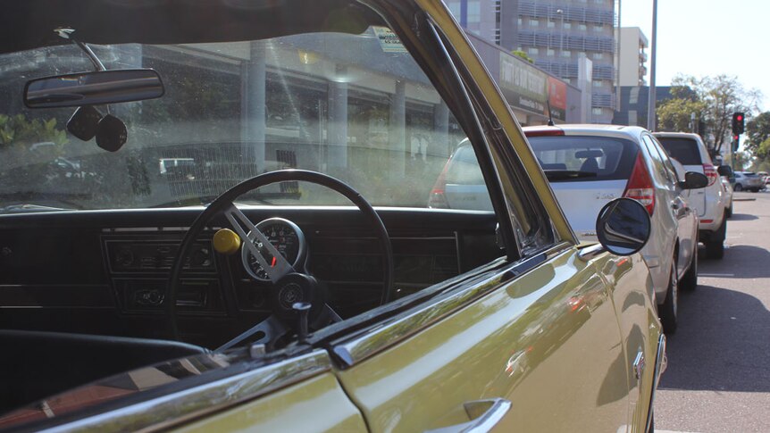 A retro Monaro car in yellow with a big steering wheel and fluffy die hanging off the rear view mirror.