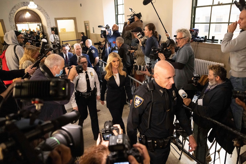 Ivanka Trump is flanked by security as she walks past throngs of photographers on either side of her in the court building.