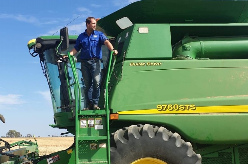 A man in a blue shirt standing on an access ladder on a large green harvester.
