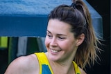 Lily Brazel, wearing a green and gold Hockeyroos uniform, smiles as she looks behind herself.