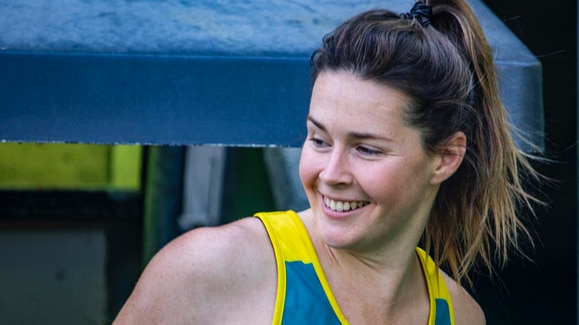 Lily Brazel, in a green and gold Hockeyroos uniform, smiles as she looks behind her.
