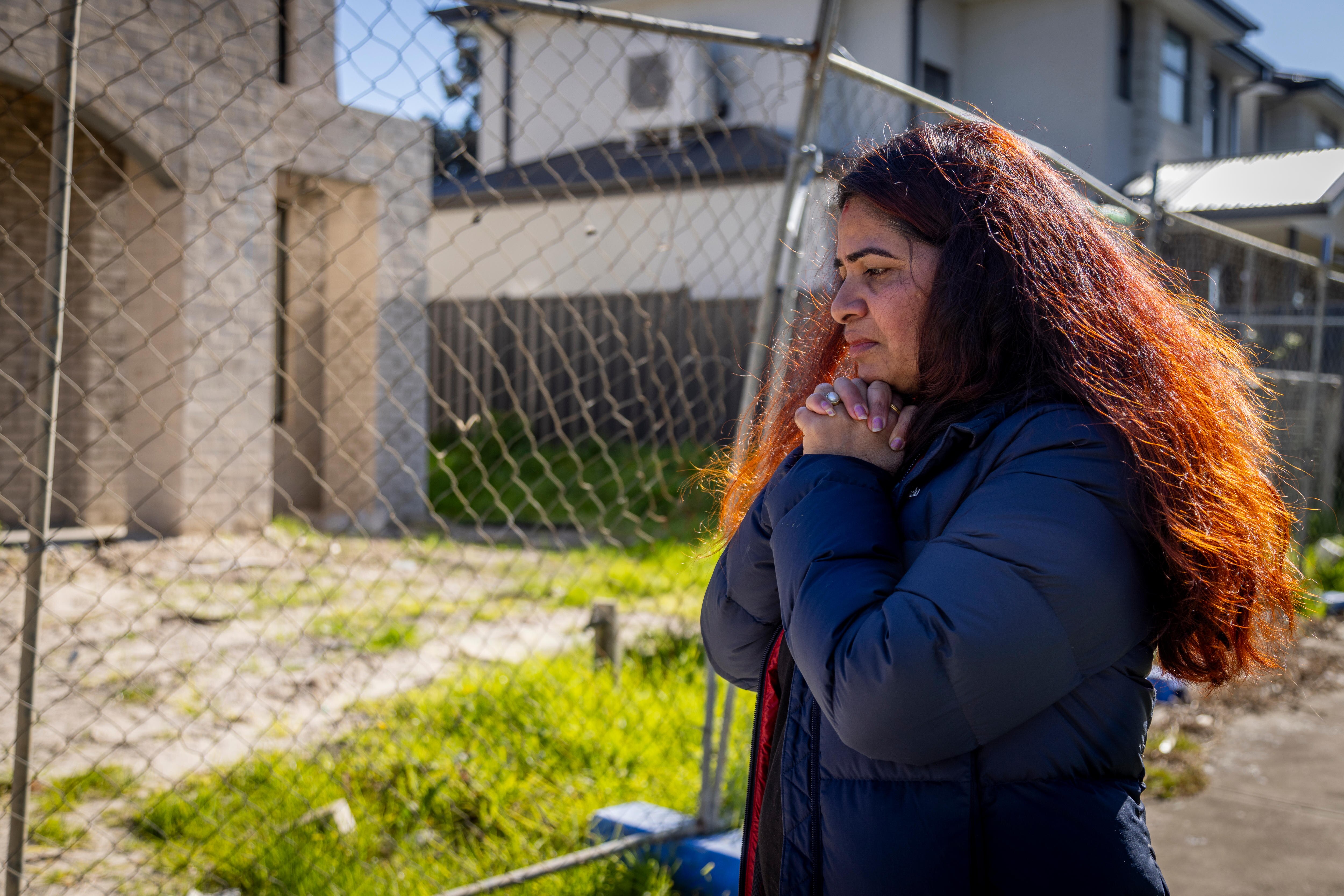 A woman standing near a fence next to an unfinished house.