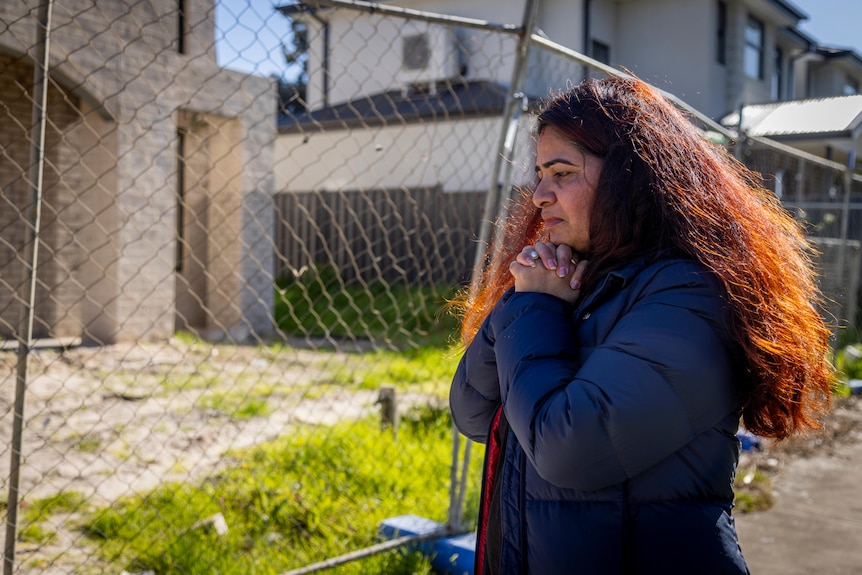 A woman standing near a fence next to an unfinished house.