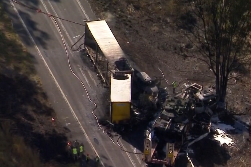 An aerial view of an articulated truck on its side after a fiery road crash.