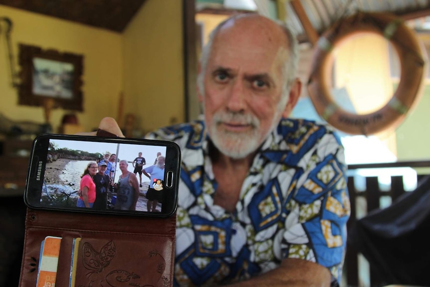 Barry Ledwidge holding up a phone displaying a recent rock sitting gathering.